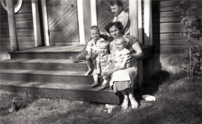 Mustavalkoinen kuva, jossa kolme lasta, mies ja nainen istuvat portailla.